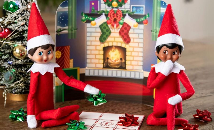 a Christmas fire place elf scene with two elves wrapping gifts.