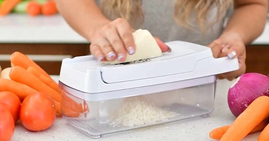 person using a clear and white vegetable chopper slicer grater to grate cheese