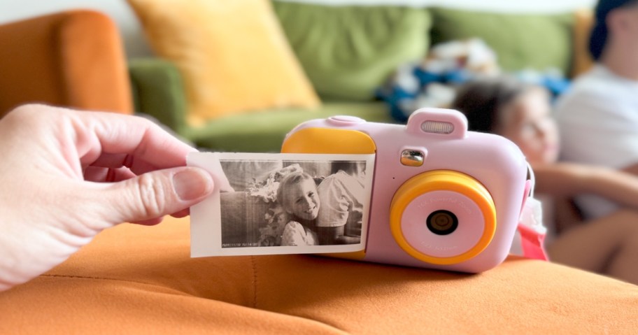 Kids instant print camera sitting on a couch while a hand holds the end of a photo being printed from the camera.