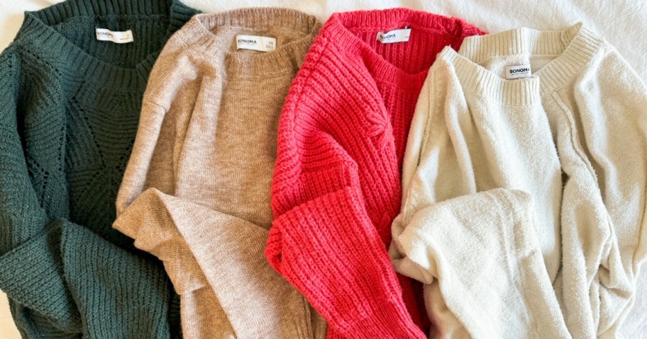 4 women's sweaters in green, tan, red, and off white on a bed