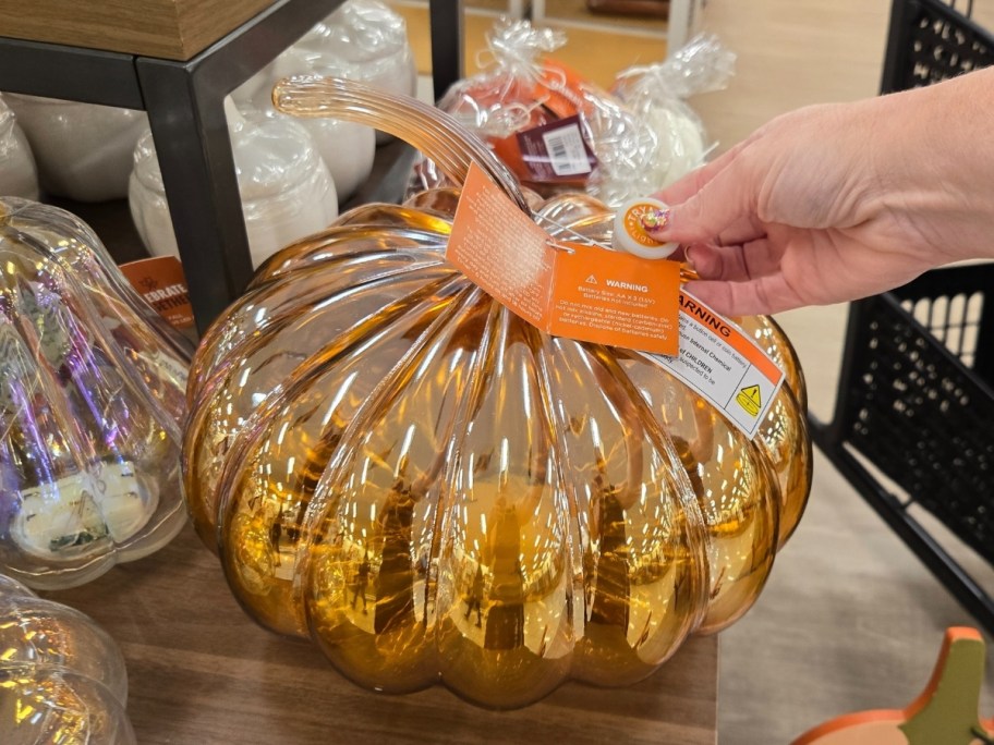 a womans hand turning on the LED lights in a large amber glass pumpkin