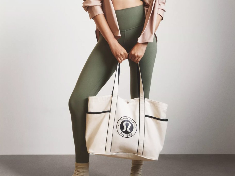 woman in green leggings holding white lululemon tote bag