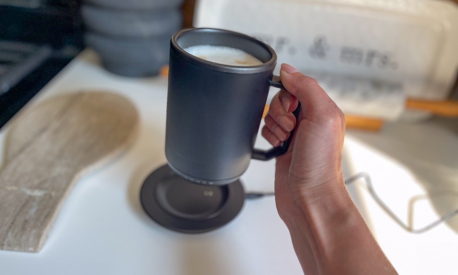 hand holding a black self warming coffee mug on white kitchen countertop