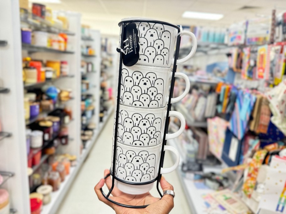 hand holding a set of 4 stacking white coffee mugs with ghosts on them in a black mug holder