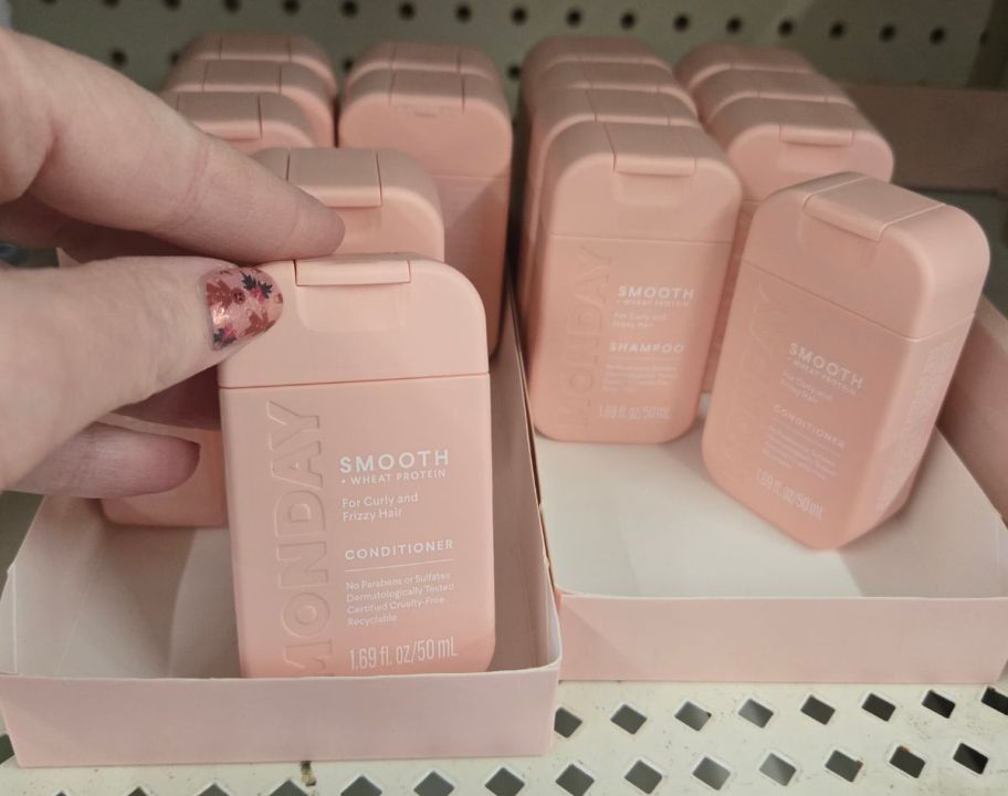 a womans hand reaching for a travel size bottle of shampoo