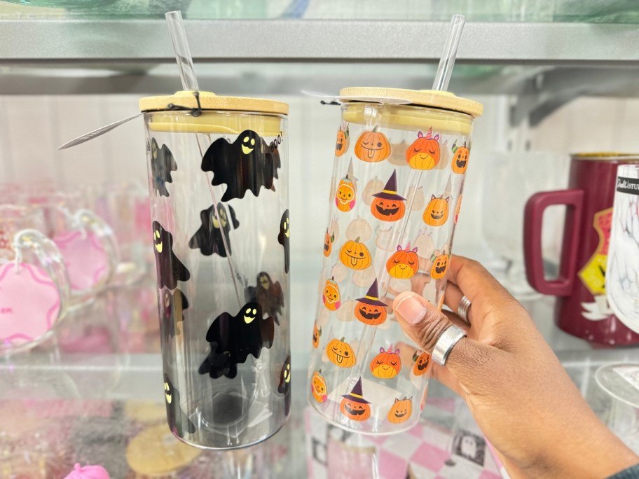 hand reaching for a tall glass tumbler with Jackolanterns on it, next to one with bats