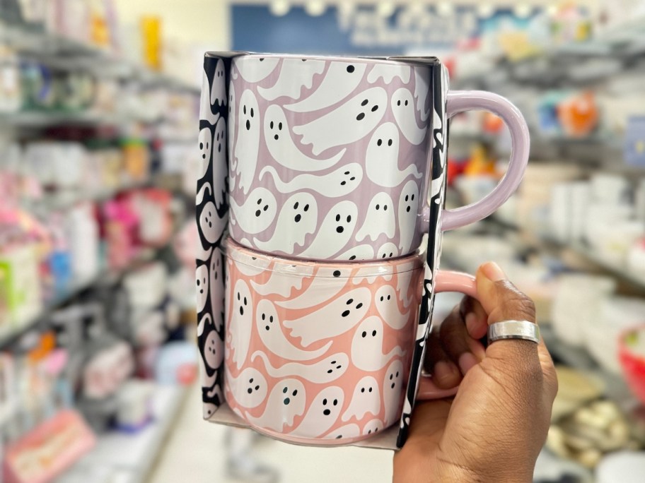 hand holding a 2 pack of coffee mugs one purple with ghosts, one pink with ghosts