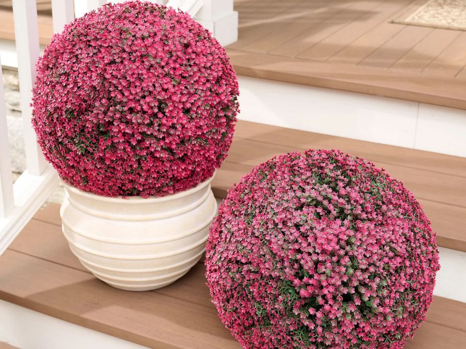 two pink mum flowers one inside a vase and another on the floor of steps