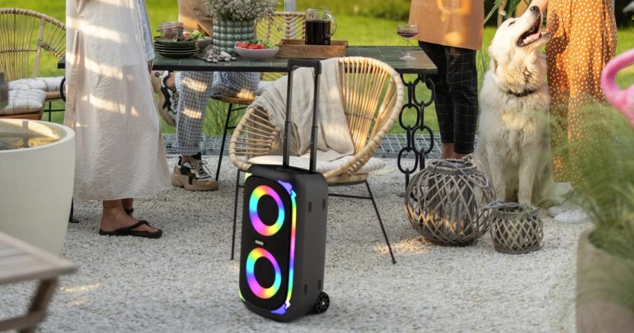 large speaker with a handle and wheels and LED lights by a table where people are having an outdoor party