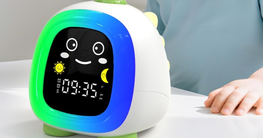 Cute dino-shaped digital clock with a smiling face, displaying 09:35. Features sun and moon icons.