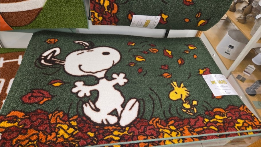 a doormat with snoopy and woodstock jumping in piles of leaves
