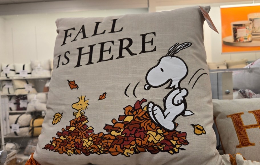 a square throw pillow with snoopy and woodstock jumping in leaves graphic