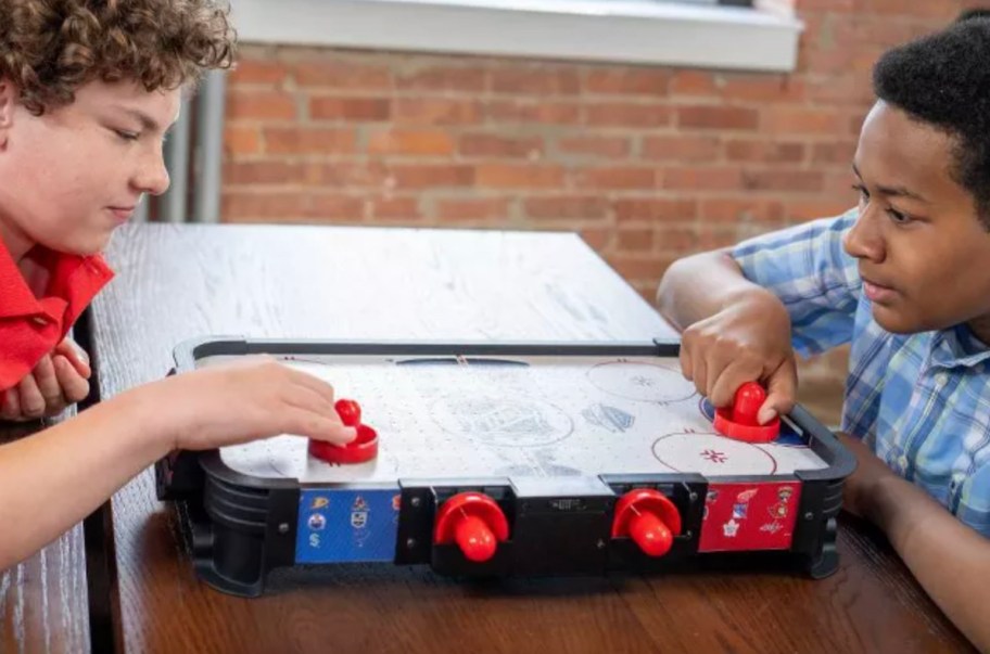 two boys playing on a tabletop air hockey game