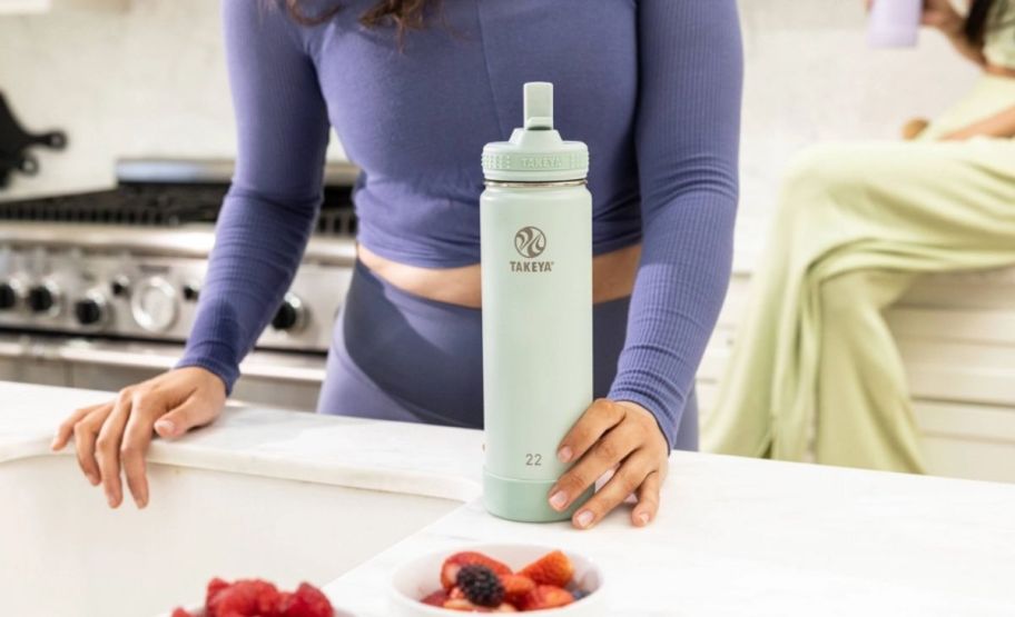 a womans hand picking up a 22 oz water bottle off a kitchen countertop