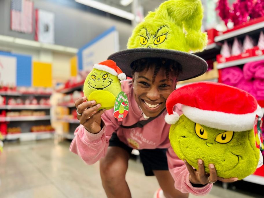 person wearing the Grinch Santa hat while holding grinch squishmallows and decorative pillow