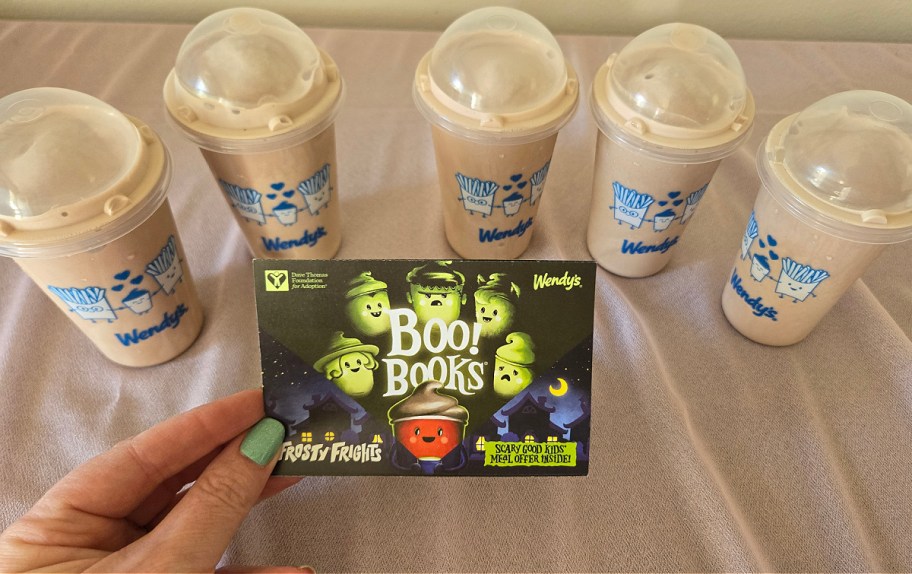 hand holding a wendys halloween boo book with coupons, with five jr frostys in the background