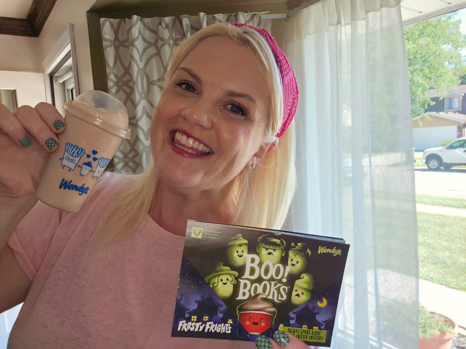 smiling woman holding a jr frosty and wendys boo book filled with halloween coupons