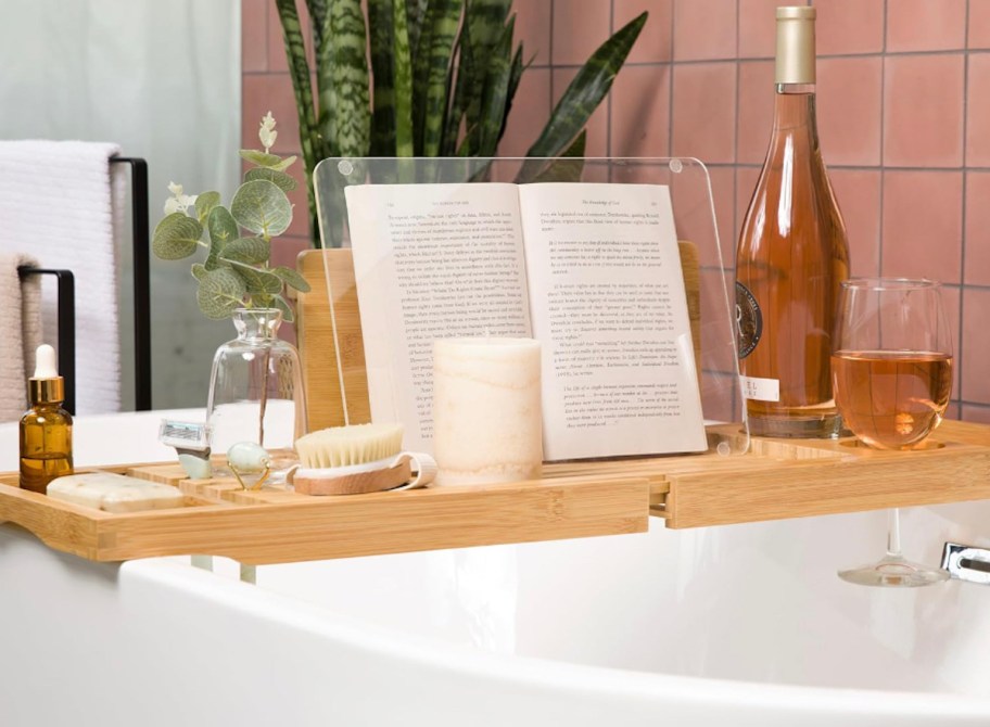 wooden bathtub tray on white bathtub filled with bubbles with book and wine bottle and glass