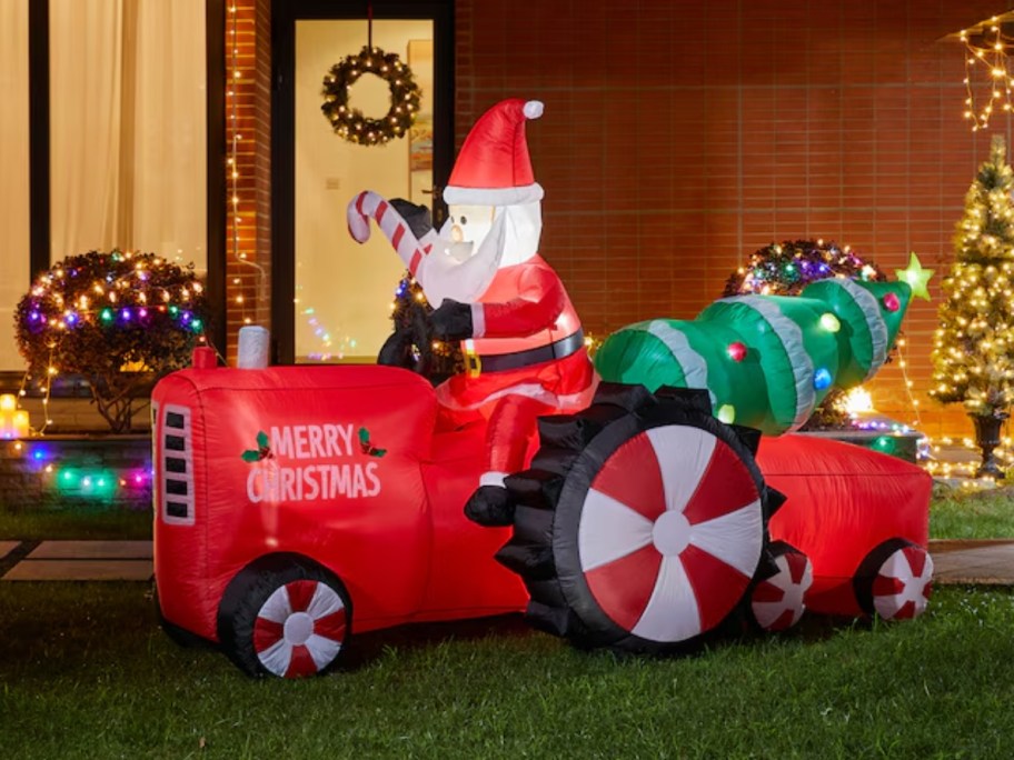 a large inflatable Santa on a Tractor with a Christmas tree Christmas decor in a front yard