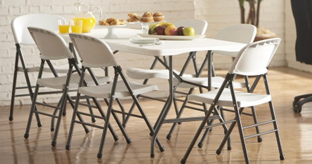 White Cosco folding table surrounded by white chairs with food on top of table