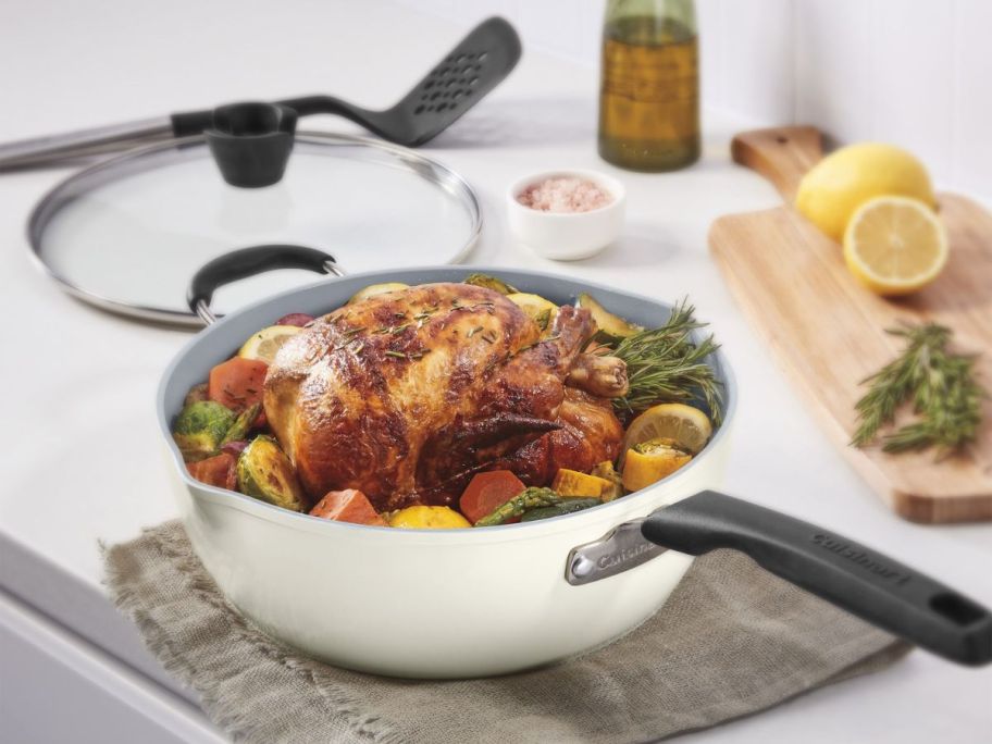 A white Cuisinart Preferred Pan with a chicken inside with the lid and a slotted spatula in the background