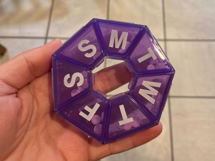 A hand holding a purple EZY DOSE Weekly Pill Organizer