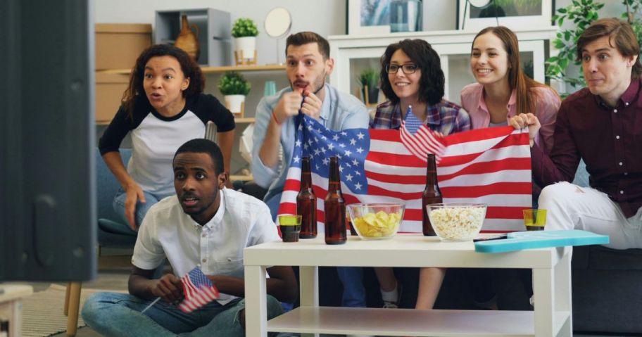 People watching TV holding an american flag and looking anxious