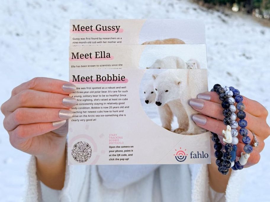 Woman holding up 3 polar bear info cards with 3 Fahlo Animal tracking bracelets on her hand