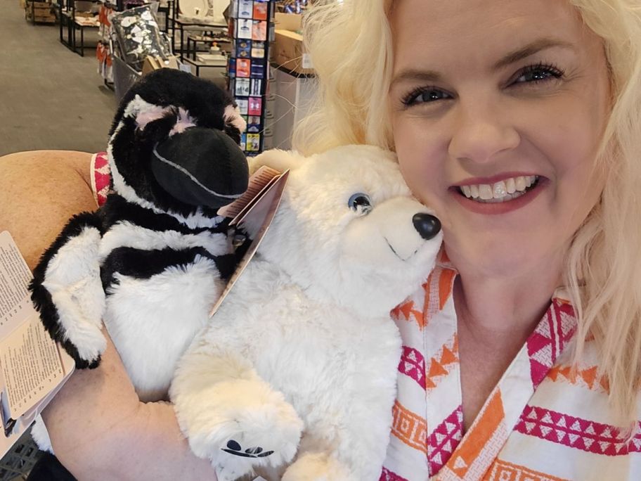 A woman holding a penguin and a polar bear stuffed animal