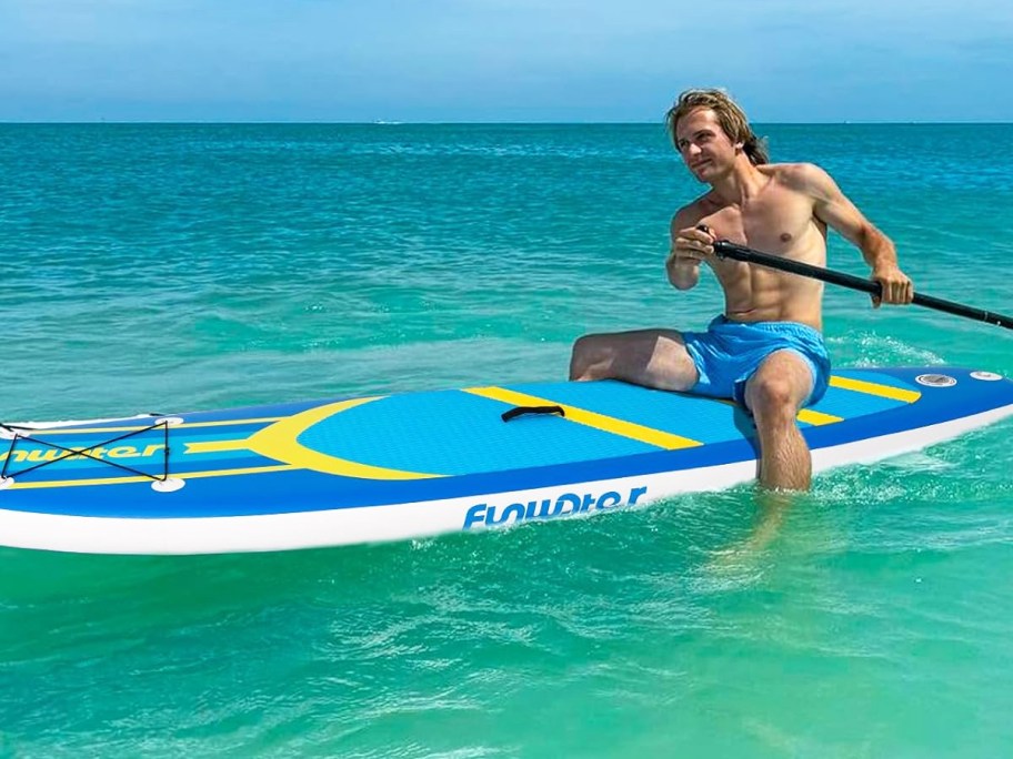 man sitting on a blue and yellow paddle board