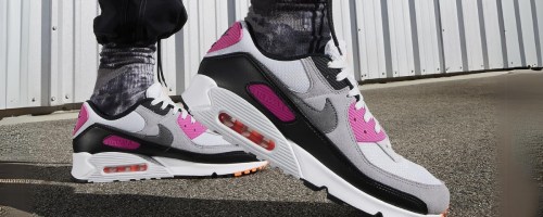 man's legs and feet wearing black Nike pants, black and white Nike socks, and black, white, grey and pink Nike Air Max shoes