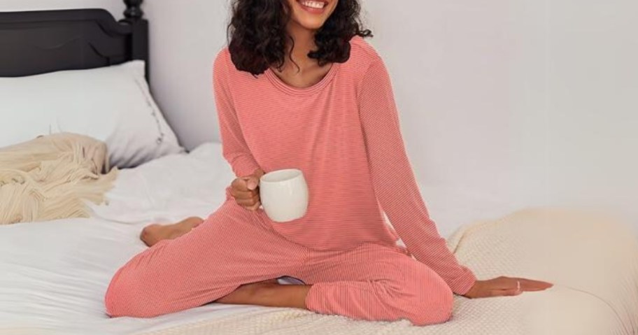 woman in a pink pajama or loungewear set sitting on a bed holding a white coffee mug