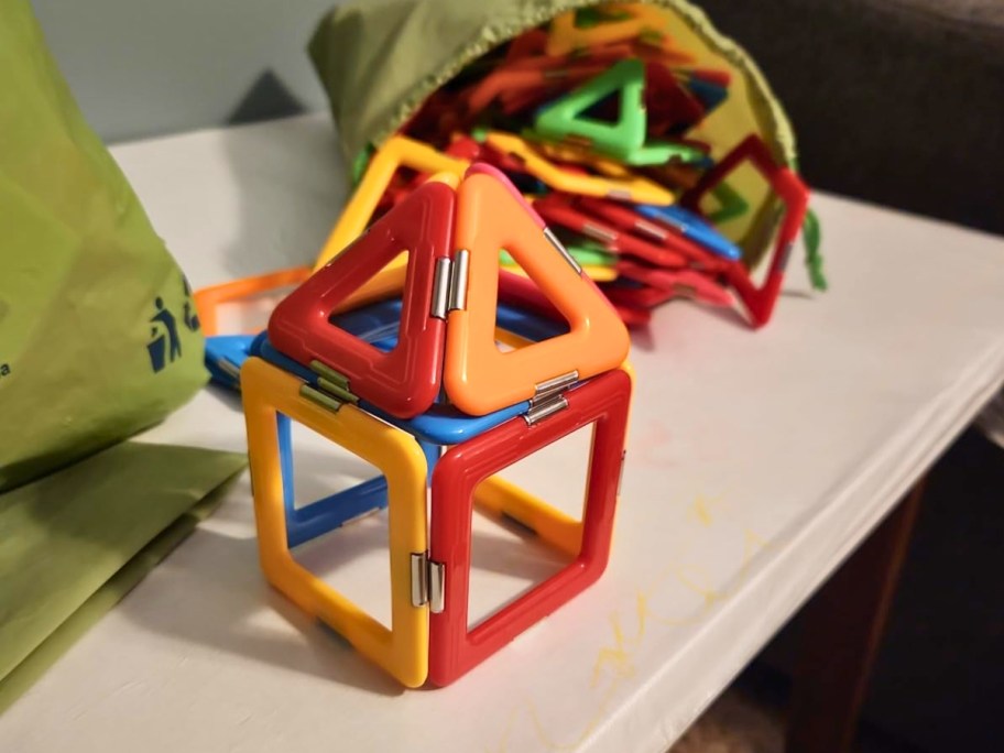 a set of colorful magnetic building tiles shaped like a house, a bag with more tiles behind it