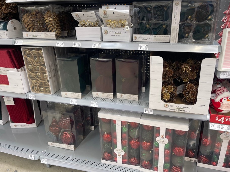 various boxes and packages of Christmas ornaments in golds, red, greens, and pinecone styles on Walmart store aisle shelves