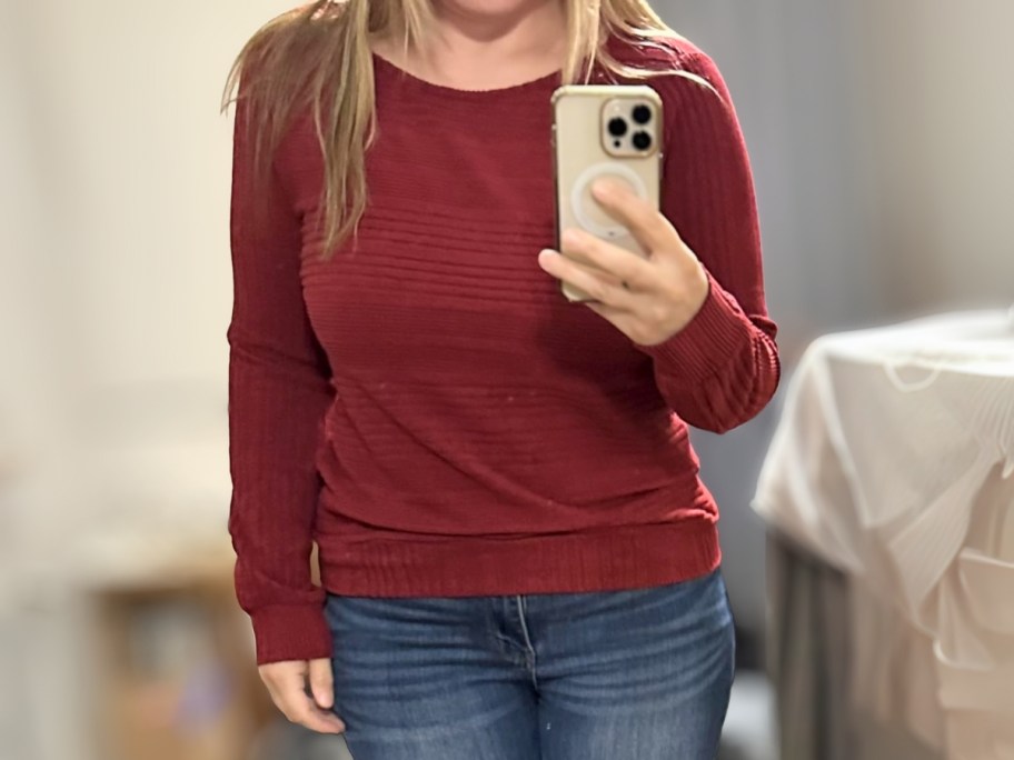 woman wearing a red ribbed top and jeans taking a selfie in a mirror