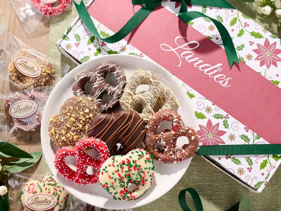 A box of Landie's Candies Stuffed Pretzels Holiday Assortment with a plate of unwrapped pretzel treats with bags of individually wrapped pretzels next to it