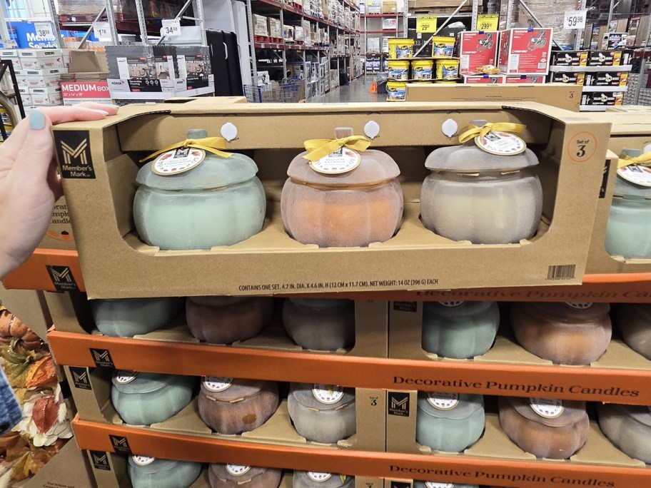 hand touching a set of glass pumpkin candles on top of a store display