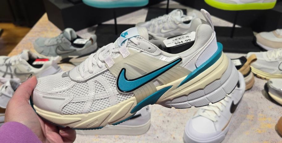 womans hand holding a white and teal nike womens sneaker