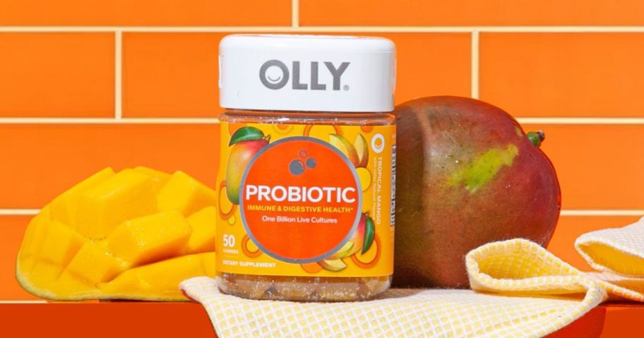 A jar of Olly Probiotic Gummy Vitamins on a shelf next to a whole and sliced mango