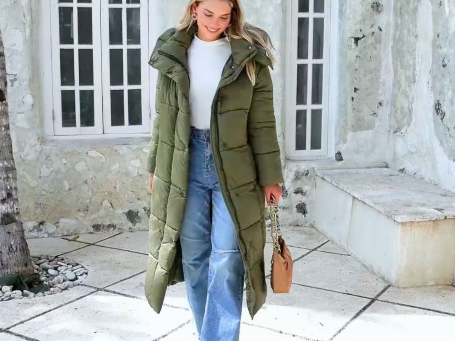 A woman wearing a long green down coat in a courtyard