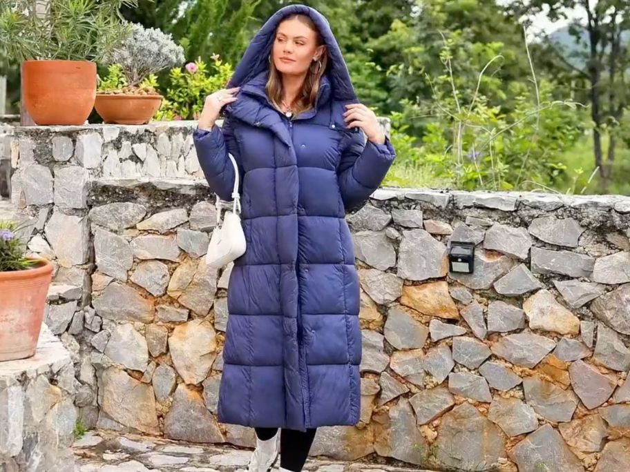 A woman in a long navy blue puffer coat standing in a garden