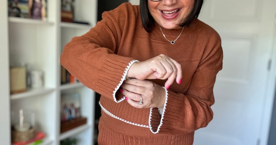 woman wearing a caramel brown color loungewear set standing in a home office holding out her arms to show the details in the top and sleeves