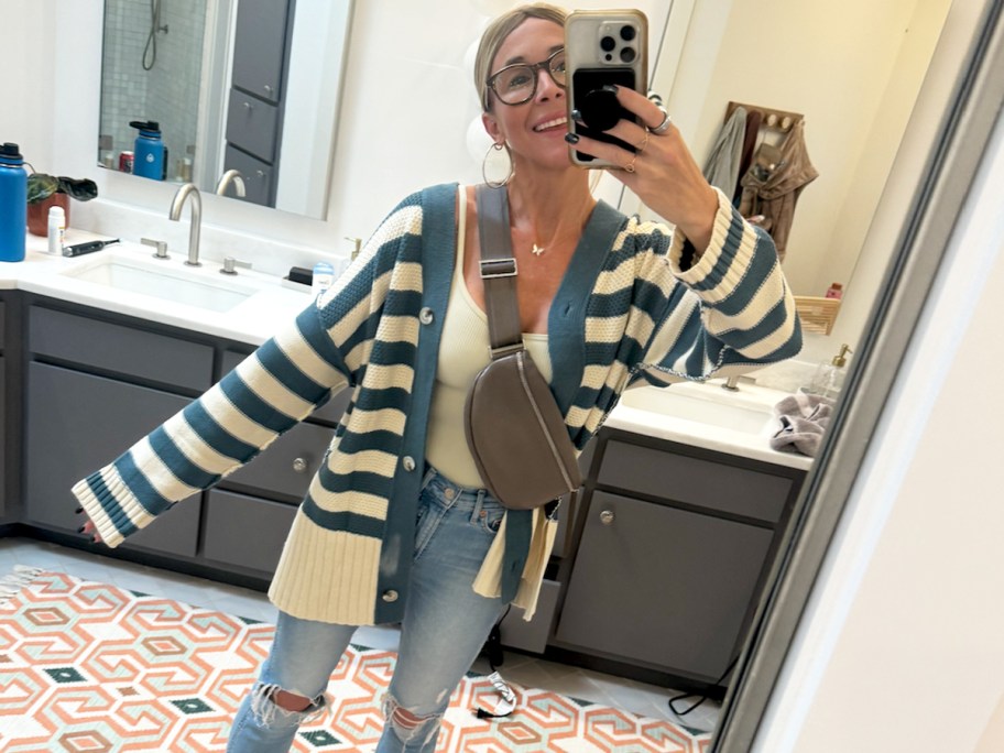 woman wearing a blue and white striped cardigan and jeans while taking photo in mirror