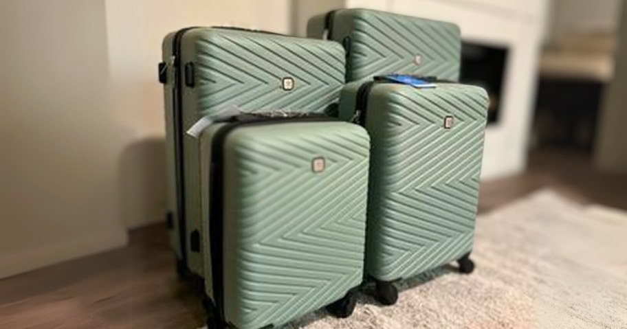 a set of 4 pieces of hardsided spinner luggage in various sizes in a sage green color in a living room