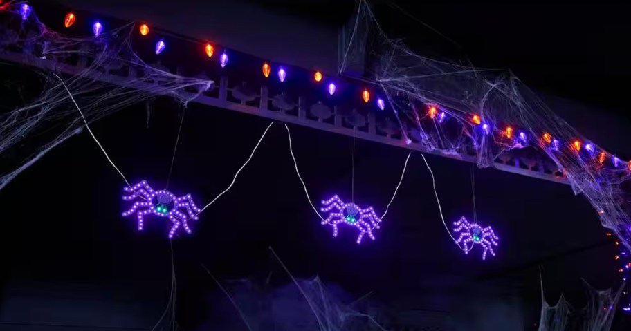 three purple led spiders hanging from house