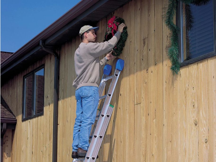 man standing on a Werner 16' Aluminum Extension Ladder hanging a holiday wreath