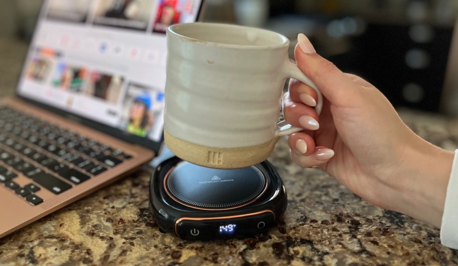 hand holding coffee mug over warming plate on granite countertop