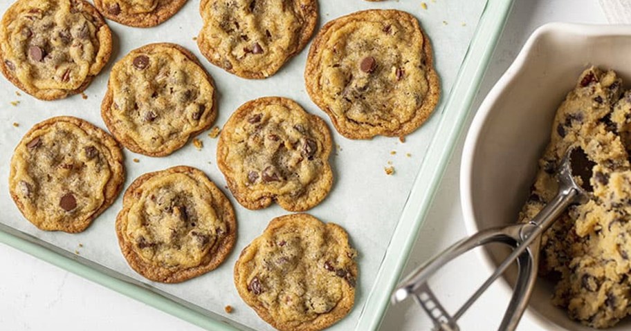 Chocolate chip cookies on baking sheet next to bowl of cookie dough