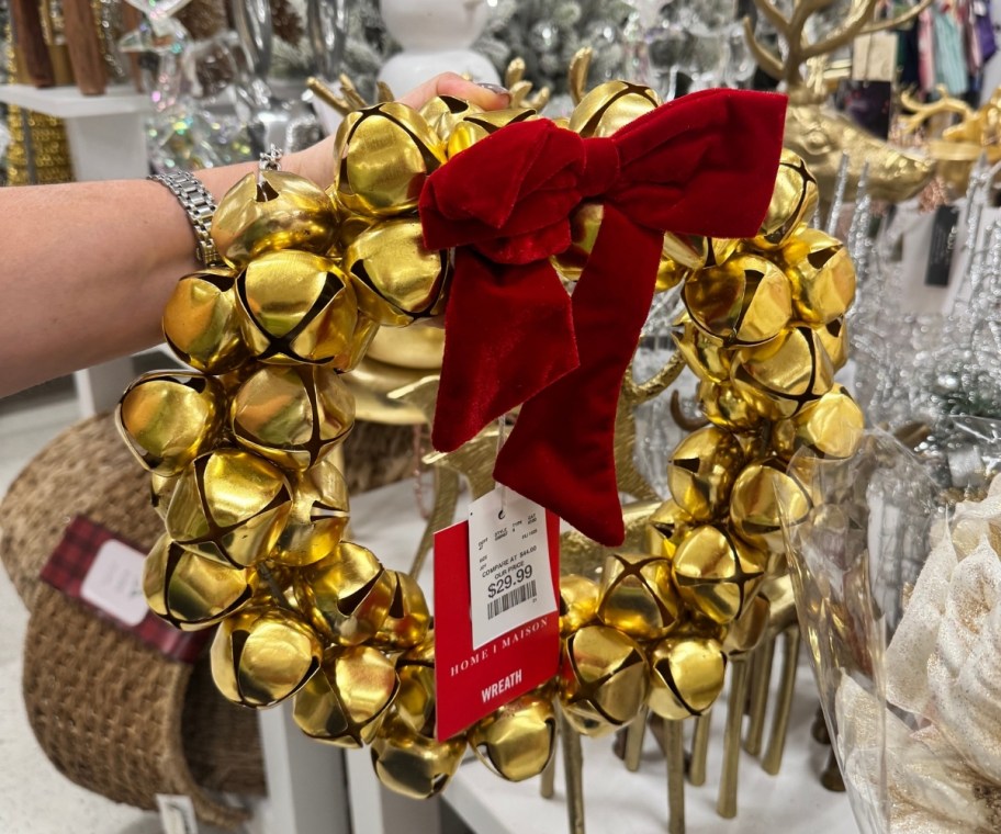 a womans hand holding a wreath made of large brass sleigh bells;. 