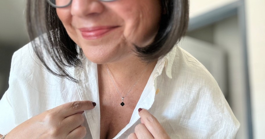 woman in a white shirt showing off a necklace with a black gemstone